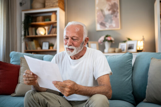 Senior man reading ANOC letter at home on sofa in living room