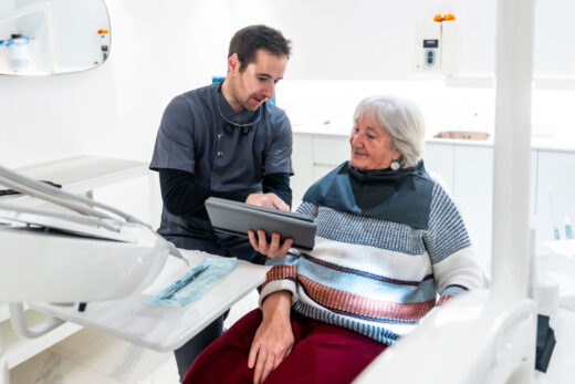 Dentist showing results on tablet to senior patient in modern clinic